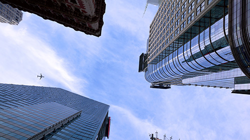 looking straight up at a plane flying in the sky between three office skyscrapers