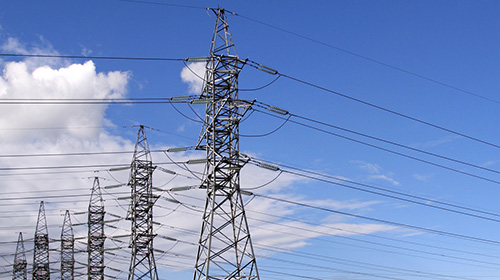 row of high voltage post transmission towers with blue sky background